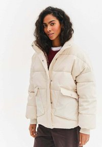 Prošívaná krémová bunda s prošívanou strukturou, dvěma předními kapsami, vysokým límcem a zapínáním na patentní knoflíky. Vhodná do chladného počasí.