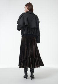 Chaqueta negra con diseño en capas, cintura elástica; falda de terciopelo marrón con textura escalonada; elegantes botas negras hasta la rodilla completan el look.