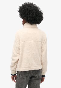 Fleece jacket in light cream with a high collar and ribbed cuffs. Textured, soft fabric with a slightly cropped hem and subtle seam details.