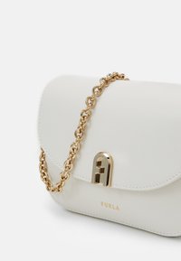 Vit läderhandväska med rundad form, guld kedjesnor och framträdande guld detaljer med varumärket "Furla" präglat på framsidan.