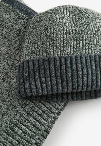 Stickad mössa och sjalset i grå nyanser, med en ribbad kant på mössan och ett strukturerat mönster på sjalen.
