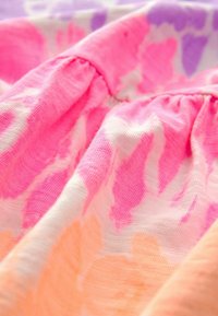 Tissu doux avec une couture élastique froncée présentant un motif floral tie-dye rose, orange et violet.
