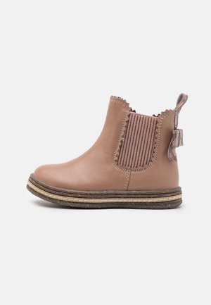 Tan leather ankle boot with ribbed elastic panel, scalloped edges, pull tab, and stacked sole with contrasting stitching and textured detail.