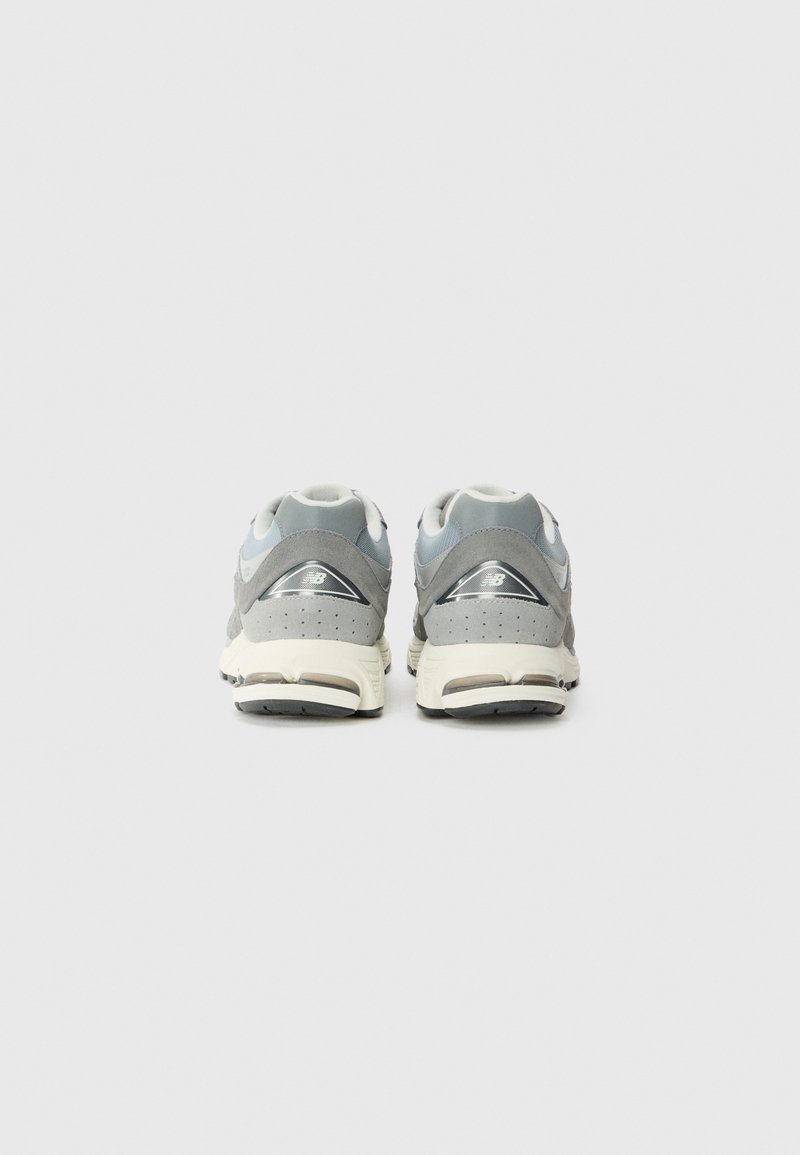 Zapatillas deportivas grises que combinan materiales de ante y malla, con una entresuela blanca y una suela de goma oscura, que exhibe detalles perforados.