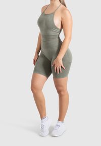 Oliwkowy bodysuit do aktywności fizycznej o dopasowanym kroju, cienkich ramiączkach i teksturowanym materiale; zestawiony z białymi butami sportowymi.