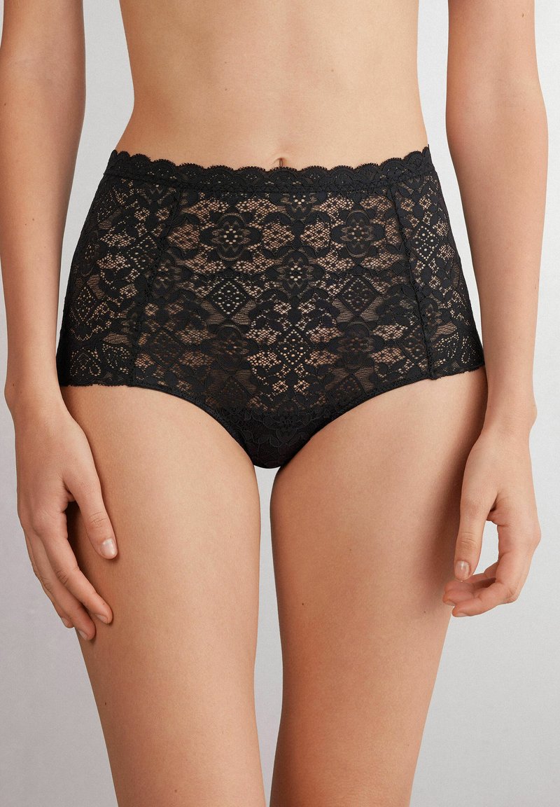 Höga svarta lace-trosor med intrikata blommönster och diamantmönster, vågiga kanter och en semi-genomskinlig textur.