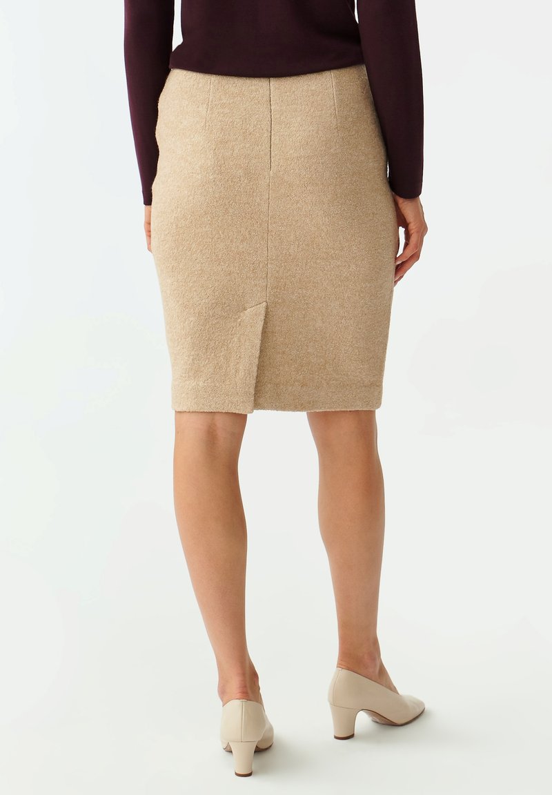 Falda lápiz de lana beige con una abertura trasera y una textura suave, combinada con tacones de color claro. Detalles de costura visibles en la cintura.