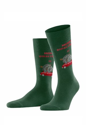 Chaussettes vertes avec une voiture rouge transportant un sapin de Noël, et le texte "Joyeux Noël" en rouge. Fabriquées dans un matériau doux et texturé.