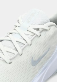 Lette atletiske sko i hvidt stof med en mesh-overdel, prydet med sølvdetaljer og flade snørebånd, med en buet form og logo-detalje.