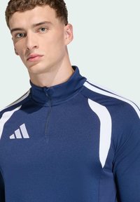 Ναυτική αθλητική μπλούζα με φερμουάρ στο λαιμό και λευκές λεπτομέρειες στους ώμους, διαθέτει ψηλό γιακά και υφή υφάσματος, με λογότυπο και τρεις ρίγες.