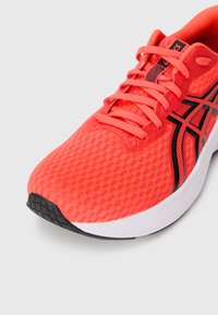 Bright red athletic shoe with a mesh upper, black accents, and textured sole. Features laces and a cushioned collar for support.