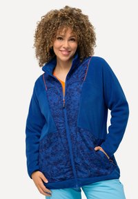 Veste en polaire bleu foncé avec des accents orange. Elle possède une fermeture éclair à l'avant, un col montant et des panneaux à motifs contrastants sur le devant.