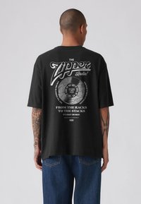 Must lühikeste varrukatega T-särk, millel on graafiline disain teksti ja vinüülplaadi illustratsiooniga tagaosas. Valmistatud puuvillast.