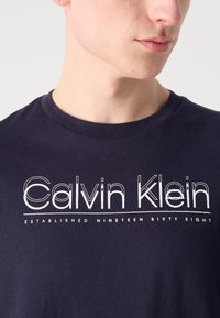 Marine-kleurige katoenen T-shirt met witte "Calvin Klein" logo-tekst in een gestileerd lettertype. Eenvoudig crew neck ontwerp, gladde textuur, geen zichtbare patronen.