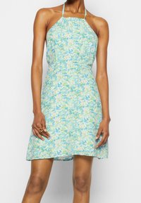 Ljusblå halterneckklänning med blommönster i nyanser av grönt och kräm, med en figurnära byst och utställd kjoldesign.