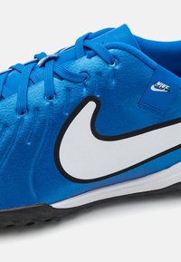 Blue synthetic sports shoe with textured upper, black sole, white Nike swoosh logo, and blue laces. Features a padded collar for comfort.
