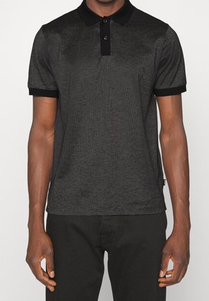 Mann trägt ein kurzärmeliges Polohemd mit schwarzem und grauem Muster, schwarzem Kragen und Bündchen, kombiniert mit schwarzen Hosen.