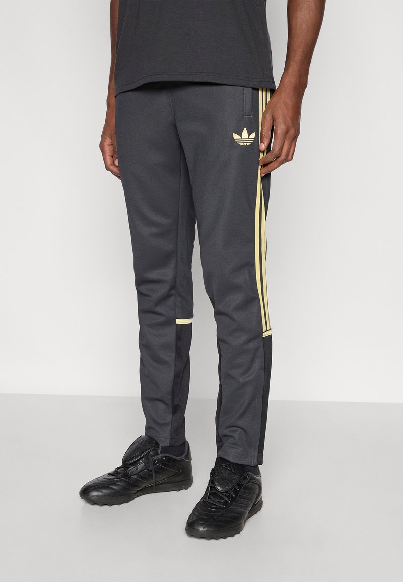 Hallid vabaajarõivad kollaste küljeribadega, millel on vasakul reiel logo ja elastsed mansetid pahkluudes. Valmistatud pehmest kangast.