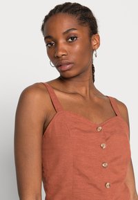 Vestido cor ferrugem com alças finas, decote coração e cinco botões de madeira na frente. Textura suave, design casual.