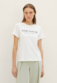 Witte katoen T-shirt met korte mouwen, met navy tekst "TOM TAILOR EST. 1962" in het midden. Gecombineerd met lichtgroene broek.