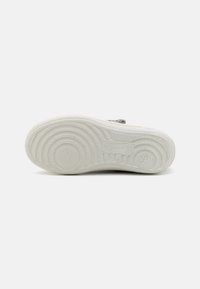 Weiße Gummisohlen von Sneakers mit kreisförmigen und gestreiften Profilmustern, ausgestattet mit geprägt Branding und einer strukturierten Oberfläche für besseren Halt.