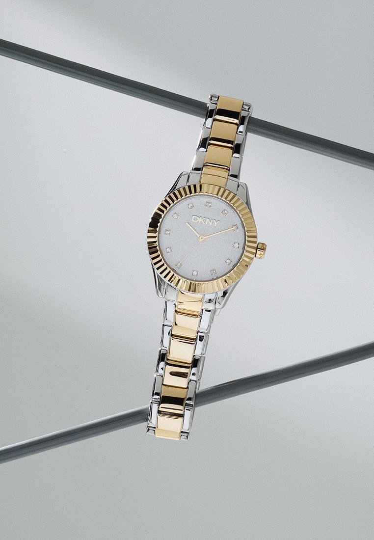 Orologio DKNY con bracciale in metallo argento e oro, quadrante bianco con indicatori in diamante, cassa arrotondata e lunetta fluted in oro.