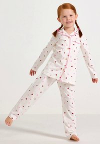 Set di pigiama bianco con maniche lunghe e pantaloni, caratterizzato da motivi a cuori rosa e rossi. Include una tasca e chiusura con bottoni. Texture morbida.