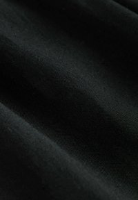 Zwarte stof met een gladde textuur, waarop subtiele lichtreflecties en kreuken zichtbaar zijn, wat wijst op flexibiliteit en zachtheid.