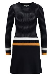 Svart stickad klänning med långa ärmar, prydd med vita och gyllene horisontella ränder över bysten och en utsvängd kjol. Mönstrad textur.