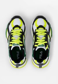 Sneakers bianchi e neri con accenti gialli, in materiale a rete, punta rotonda e colletto imbottito; presentano dettagli verdi prominenti e lacci.