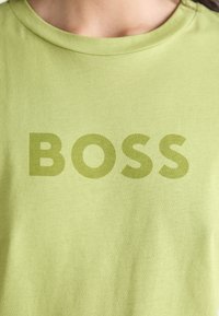 Light green cotton t-shirt featuring a large, bold "BOSS" printed in a slightly darker green shade. Smooth texture, crew neck design.