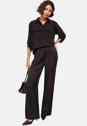 Schwarz, übergroße Bluse mit zwei Brusttaschen und hochgekrempelten Ärmeln, kombiniert mit hoch taillierten, weit geschnittenen Hosen. Glattes Material und minimalistisches Design.