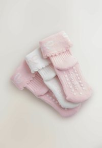 Tri páry zložených detských ponožiek v ružovej a bielej farbe so zvlnenejšími lemmi a protišmykovými bodkami na podrážkach, usporiadané do diagonálneho stohu.