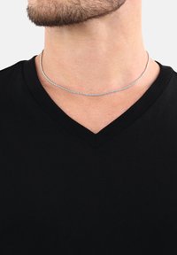 Collana in argento su collo nudo, con un design attorcigliato. Indossata su una maglietta nera a V, mette in risalto la lucentezza della collana.