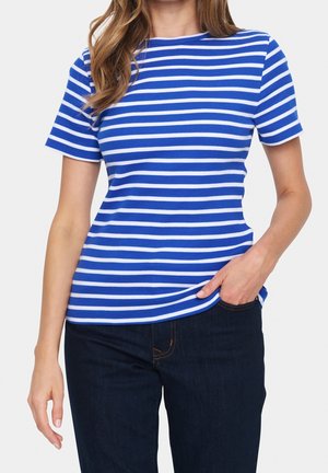 Vrouw die een blauw-wit horizontaal gestreept T-shirt met korte mouwen draagt, licht in een donkerblauwe jeans gestopt, met één hand in de zak.