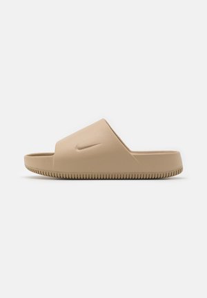Enkelt beige Nike slide sandal med bred rem og tekstureret sål, vist fra siden på en hvid baggrund.