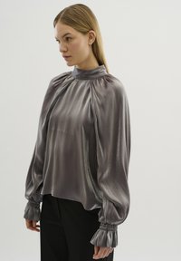 Zijdeachtige, lichtgrijze blouse met een hoge hals, geplooide details en gathered, gerimpelde cuffs. Losse pasvorm, gladde textuur.