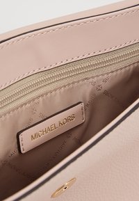 Primo piano dell'interno di una borsa in pelle beige che mostra una tasca con zip, l'etichetta del logo Michael Kors e la fodera in tessuto beige con stampa del marchio.