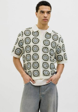 Short-sleeve shirt with crochet pattern in cream, olive green, and light blue. Features a collar and front zip, made from textured fabric.