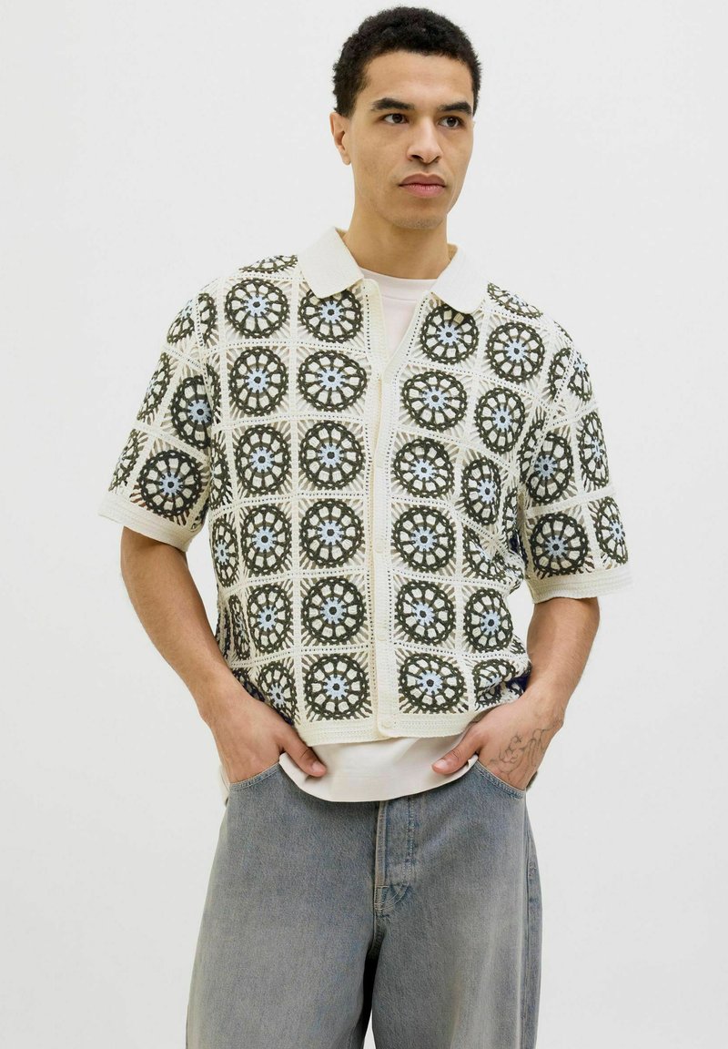 Kratka majica s kratkimi rokavi in crochet vzorcem v kremni, olivno zeleni in svetlo modri barvi. Ima ovratnik in sprednji zadrgo ter je izdelana iz teksturirane tkanine.