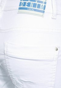 Jean de mezclilla blanca con un bolsillo trasero con un acento metálico y una etiqueta azul con el texto "LOVE DENIM CECIL". Textura suave.