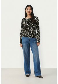Black long-sleeve top with beige polka dots, paired with high-waisted blue wide-leg jeans and black pointed-toe shoes.