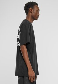 Black oversized cotton t-shirt with short sleeves, featuring a white graphic design of stars on the left side. Finished with a round neckline.
