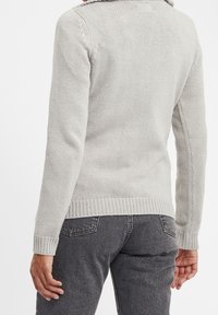 Maglione a maglia grigio chiaro con orlo e polsini a coste, colletto ripiegato e trama testurizzata. Indossato con jeans grigi scuri.
