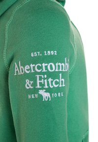 Grøn sweatshirt med hætte, der har hvidt broderet tekst: "Abercrombie & Fitch EST. 1892 NEW YORK" og et lille moskusokse-logo.