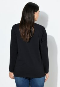 Schwarzes Langarm-T-Shirt aus weichem Stoff, mit abgerundetem Saum und minimalistischer Gestaltung, kombiniert mit blauen Jeans. Rückansicht dargestellt.