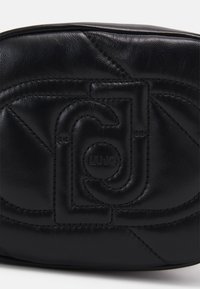 Zwarte leren tas met reliëflogo, gequilt ontwerp en zichtbare stiksels. Compact rechthoekig van vorm met een gladde textuur.