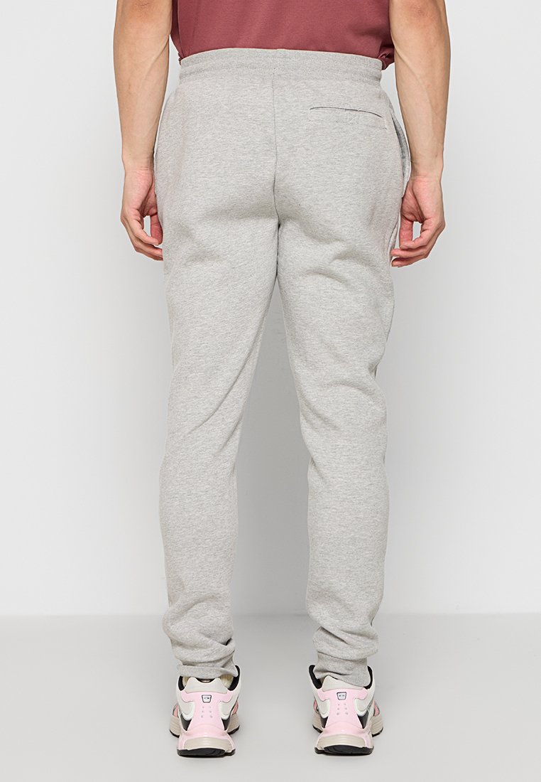 Pantalones de chándal gris claro con forma ajustada, cinturilla elástica y un bolsillo trasero. Llevados con zapatillas rosas y negras.