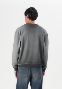 Grå sweatshirt med et gradvist faldefarve-design, ribbede ærmer og talje. Slim fit med rå kantdetalje, parret med blå jeans.