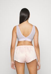 Bralette cinza com alças largas e costas em V profundo, combinado com calções de seda rosa claro com cintura elástica e bainha curva.